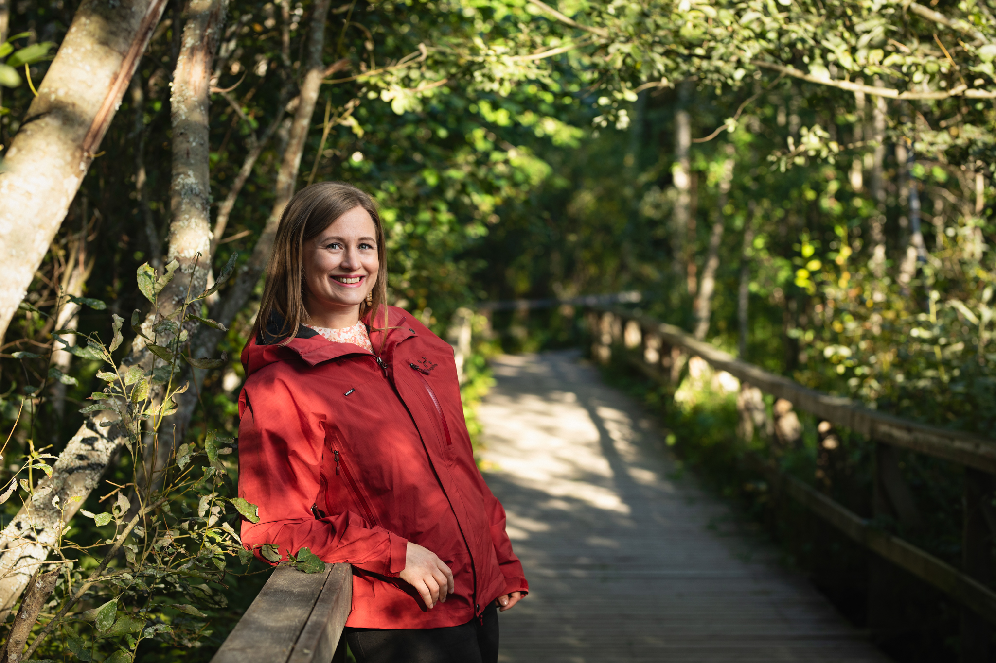 Olga Gilbert nojaa vehreässä ympäristössä sillankaiteeseen ja hymyilee avoimesti ja kuuntelevasti