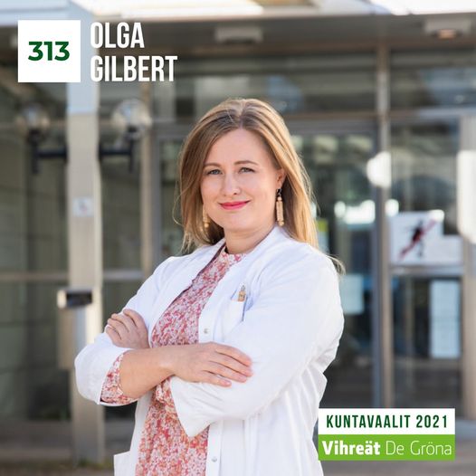 Lääkäri ja kuntavaaliehdokas Olga Gilbert numerolla 313 seisoo kädet päättäväisesti puuskassa ja hymyilee suoraan kohti katsojaa